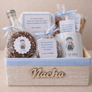 Desayuno fallero personalizado en caja de tela beige con nombre en madera, taza con ilustración de fallero, dulces tradicionales y tarjeta dedicada en tonos azul pastel.