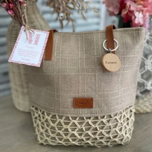 Bolso de tela en tonos neutros con detalle de red en la parte inferior, placa de madera personalizada con el nombre "Carmen", etiqueta con mensaje para mamá y ramillete de flores secas.