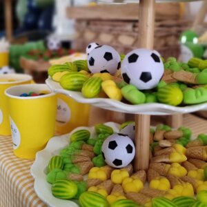 Balones de fútbol pequeños sobre chuches verdes y amarillas de la mesa dulce de Canella en Rama
