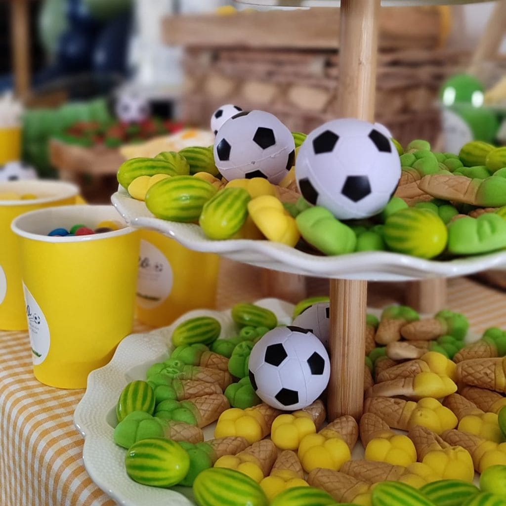 Balones de fútbol pequeños sobre chuches verdes y amarillas de la mesa dulce de Canella en Rama