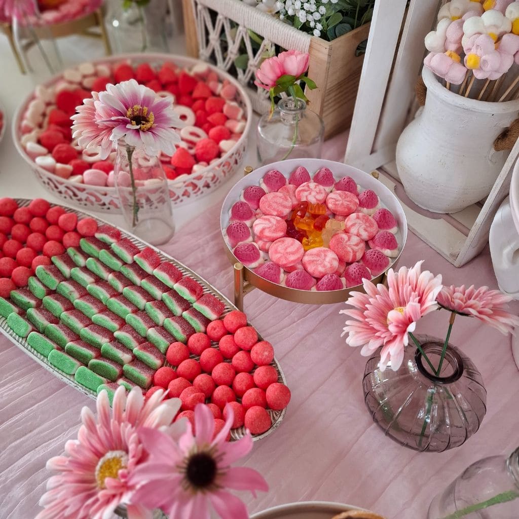 Mesa de chuches para boda en tonos rosas y verdes, con bandejas de golosinas y decoración floral