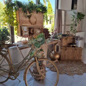 Mesa dulce rústica para boda con bicicleta dorada, decoraciones de madera y vegetación