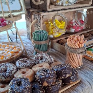 Detalle de mesa dulce rústica para boda con donuts, chuches en frascos y decoración natural