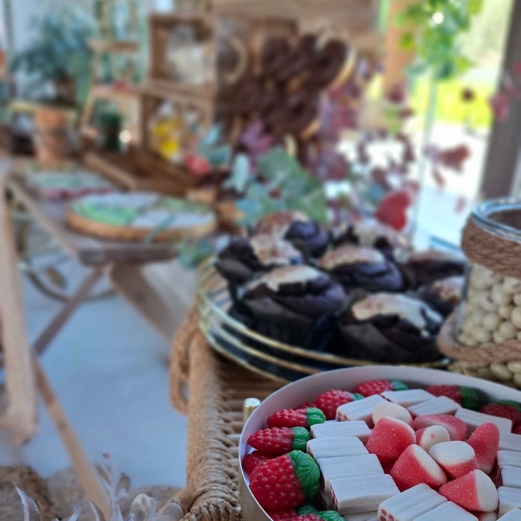 Mesa dulce rústica con muffins, chuches rojas y verdes en decoración natural para bodas
