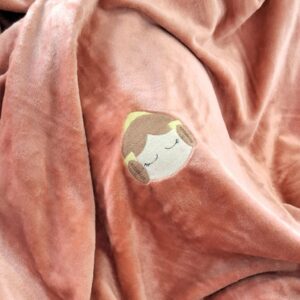 manta de fallera rosa con una cara de fallera bordada en el centro sobre un sofa