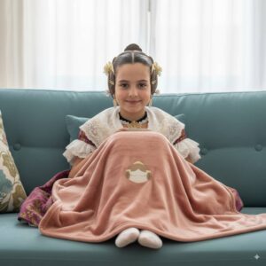 fallera infantil sentada en sofa utilizando la manta fallera de Canella