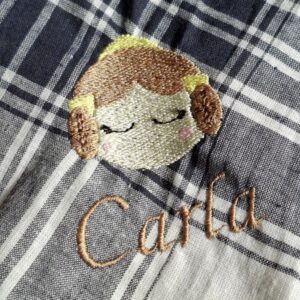Primer plano de un pañuelo fallero de cuadros con bordado personalizado de una fallera y el nombre "Carla".