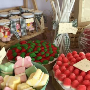 Detalle de mesa dulce con botes de cristal llenos de chuches decorados con lazos de cuadros vichy en tonos verdes. Acompañado de carteles ilustrados personalizados y una cuidada presentación de chuches en recipientes de madera y cristal.