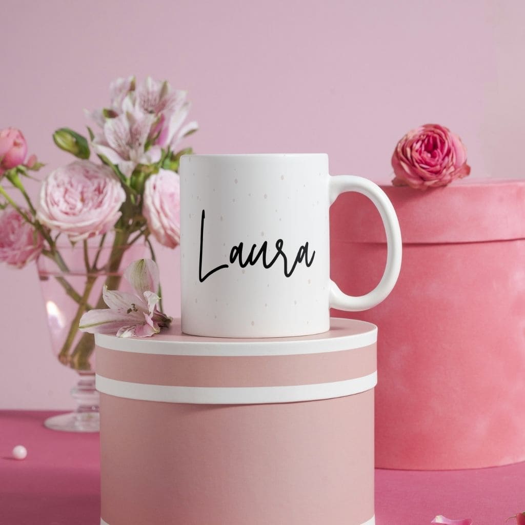 Taza de corazones personalizada con el nombre Laura presentada en un elegante escenario rosa con flores y cajas decorativas de la colección de San Valentin