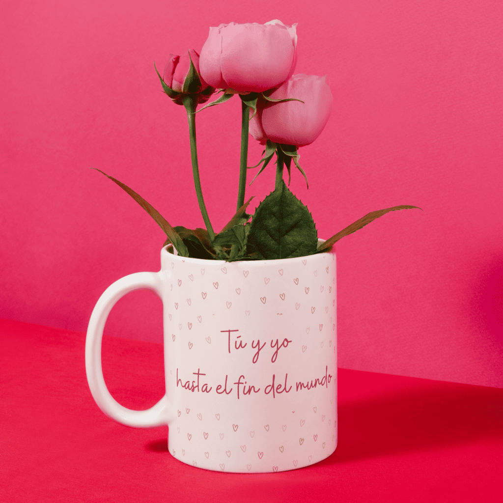 Taza con la frase "Tú y yo hasta el fin del mundo" utilizada como jarrón decorativo con rosas rosas.