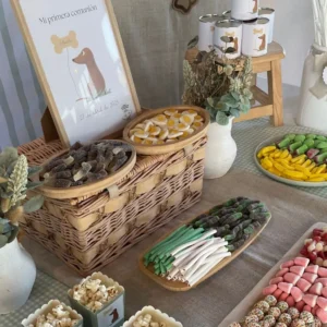 Plano cercano de chuches surtidas sobre cesta de mimbre en una mesa dulce de comunión con decoración de perrito salchicha y cartel personalizado.