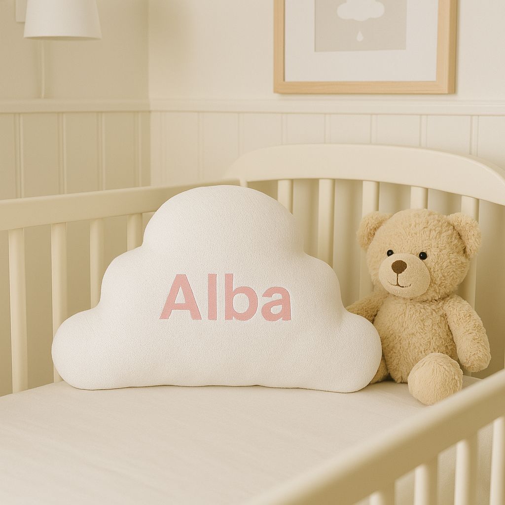 Cojín para recién nacida en forma de nube dentro de una cuna, junto a un peluche de osito.