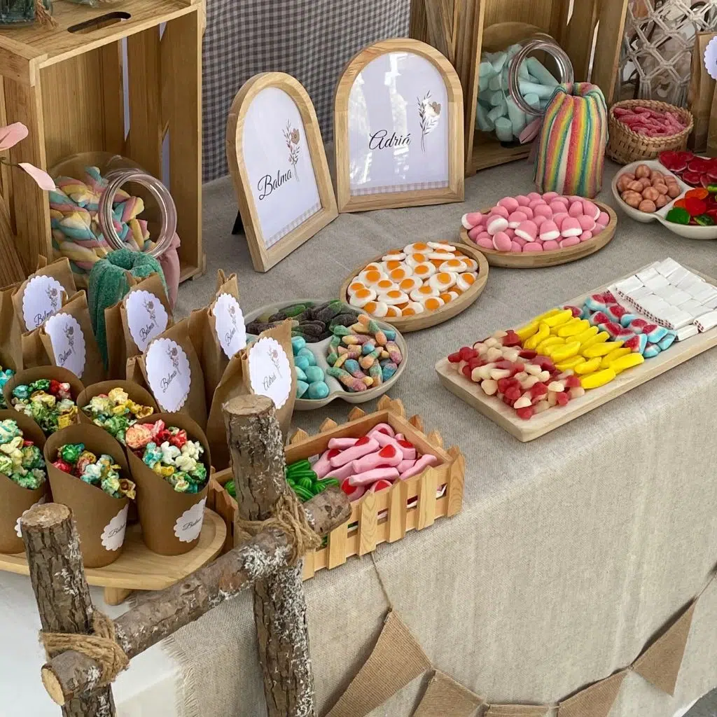 Detalle de la mesa dulce beige con golosinas variadas, conos personalizados y marcos con nombres.