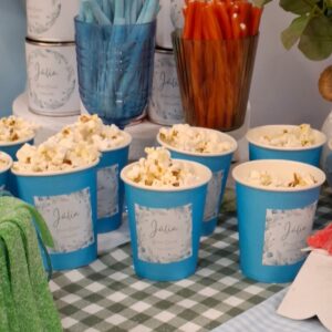 Vasos personalizados con palomitas en mesa dulce para primera comunión con temática azul y verde.