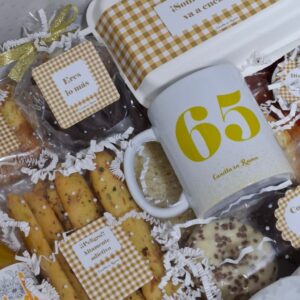 Caja de desayuno de cumpleaños de Canella en Rama con detalles personalizados, productos dulces y taza con número 65 en amarillo, ideal para regalar.