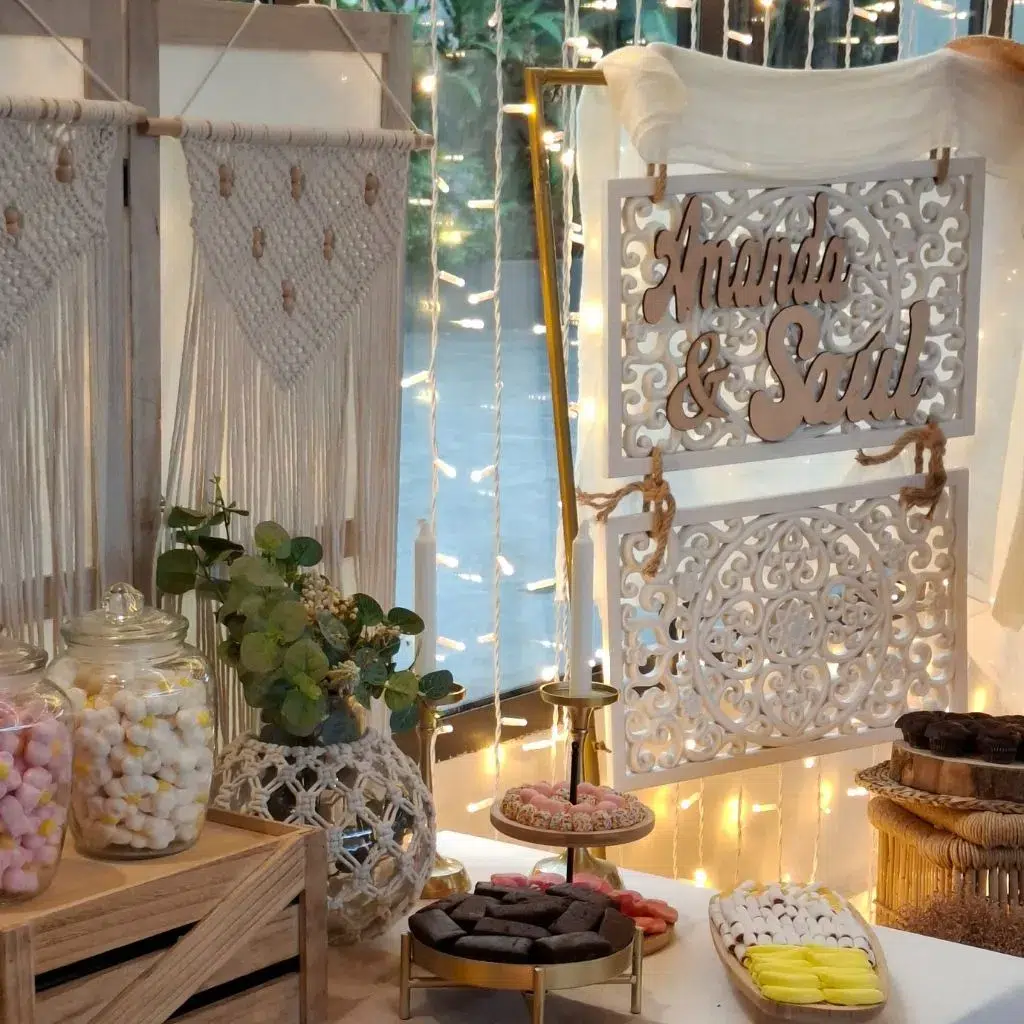Mesa dulce estilo Ibiza con cartel personalizado Amanda & Saúl, dulces y luces de fondo